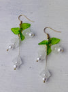 front of delicate bell flower drop earrings with soft white petals and green leaf details.