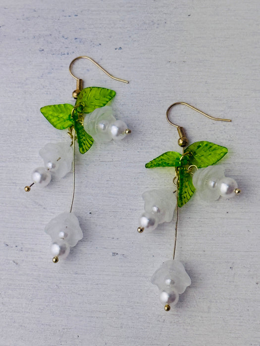 front of delicate bell flower drop earrings with soft white petals and green leaf details.