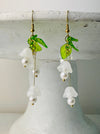 pair of delicate bell flower drop earrings with soft white petals and green leaf details.