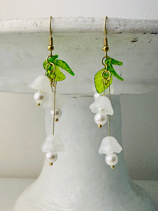 pair of delicate bell flower drop earrings with soft white petals and green leaf details.