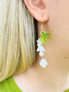 close-up of delicate bell flower drop earrings with soft white petals and green leaf details.