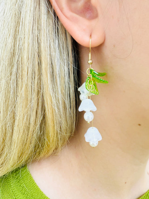 close-up of delicate bell flower drop earrings with soft white petals and green leaf details.