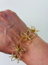 Delicate gold-tone floral bracelet with linked open-petal flower design and adjustable chain extender, displayed on a model.
