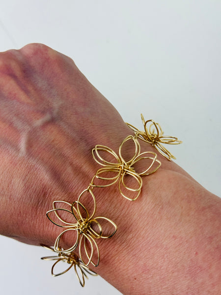 Delicate gold-tone floral bracelet with linked open-petal flower design and adjustable chain extender, displayed on a model.