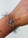 Delicate silver-tone floral bracelet with linked open-petal flower design and adustable chain extender, displayed on a model.