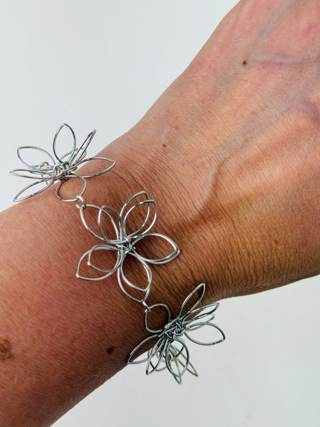 Delicate silver-tone floral bracelet with linked open-petal flower design and adustable chain extender, displayed on a model.