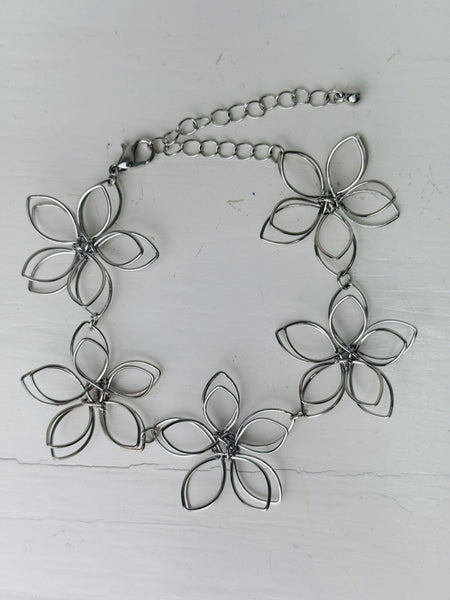 Delicate silver-tone floral bracelet with linked open-petal flower design and adustable chain extender, displayed on a white background.