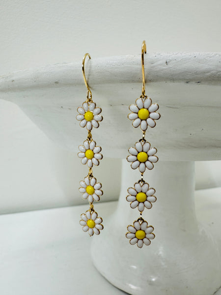 A pair of floral dangle earrings with white and yellow flowers on a gold-colored chain, displayed against a light background.