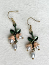 Pair of earrings with floral and pearl designs on a textured white background