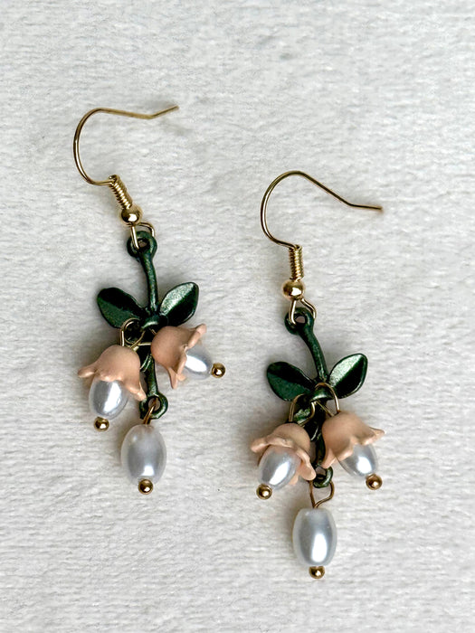 Pair of earrings with floral and pearl designs on a textured white background