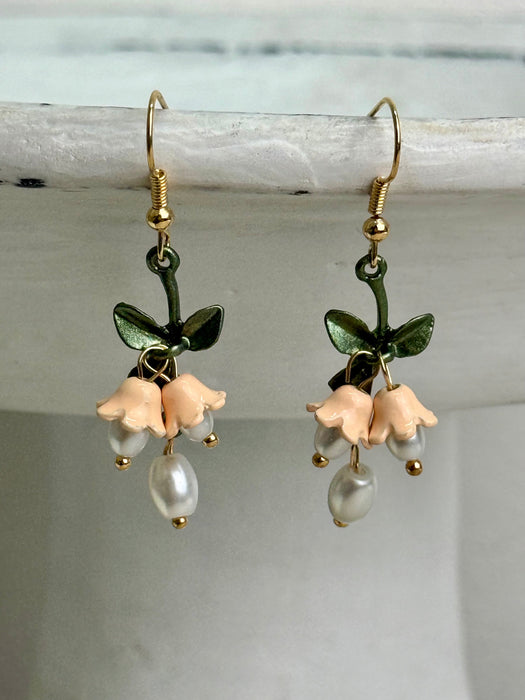 Pair of floral earrings with green leaves and beige flowers on a light background