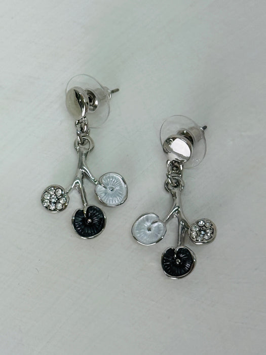 White and grey floral enamel drop earrings with crystal effect glass stones on a silver-tone branch design, dispayed on a table.