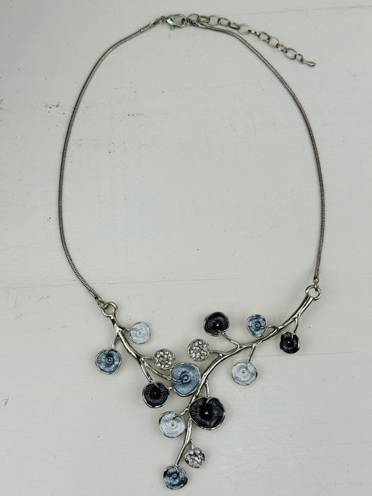 White and dark grey floral enamel necklace with crystal effect glass stones an a silver-tone chain, displayed on a table.