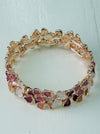 Gold-tone stretch bracelet with small enamel flowers in cream and rose gold on a white background.