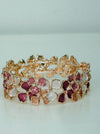 Gold-tone stretch bracelet with small enamel flowers in cream and rose gold on a white background.