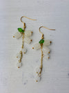 A pair of elegant drop earrings with frosted white floral beads, translucent accents, and green leaf details, on a gold-colored chain.
