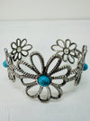 A silver-colored flower-style cuff bracelet with a turquoise stone in the centre, displayed on a white background.
