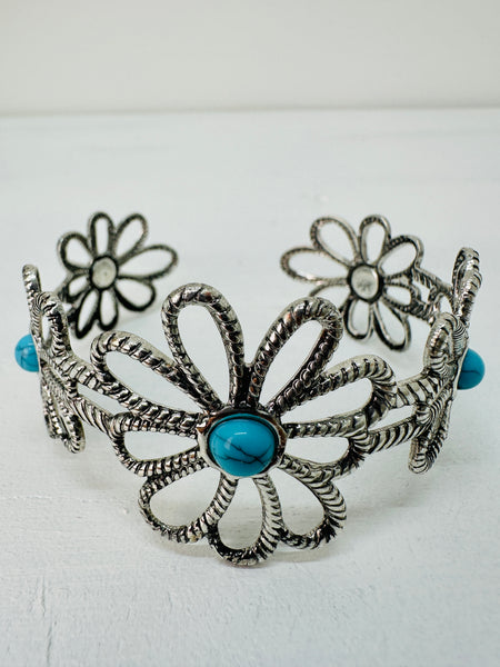 A silver-colored flower-style cuff bracelet with a turquoise stone in the centre, displayed on a white background.