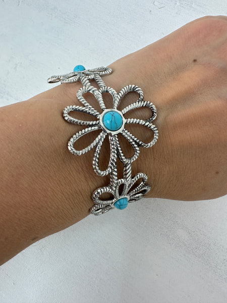 A silver-colored flower-style cuff bracelet with a turquoise stone in the centre, displayed on a model.