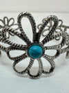 Close -up silver-colored flower-style cuff bracelet with a turquoise stone in the centre, displayed on a white background.