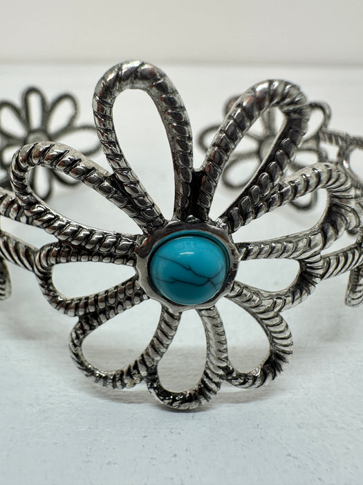 Close -up silver-colored flower-style cuff bracelet with a turquoise stone in the centre, displayed on a white background.