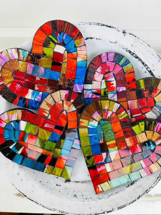 Group of Fragaria heart-shaped mosaic coasters with colourful hand-painted glass pieces on MDF bases, photographed from above on a light textured surface.