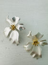 Elegant pearl white flower stud earrings with a gold-tone centre, displayed on a table.