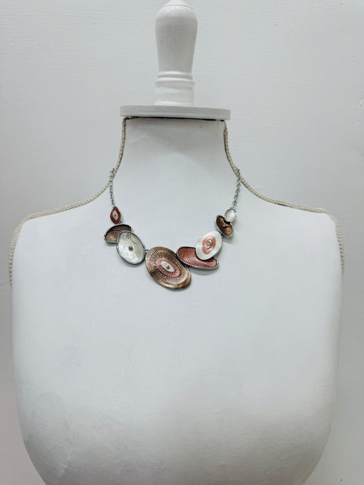 Geometric statement necklace with silver tone chain and enamelled oval elements in bronze and pearl shades displayed on a mannequin.