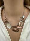 Geometric statement necklace with silver tone chain and enamelled oval elements in bronze and pearl shades displayed on a model.