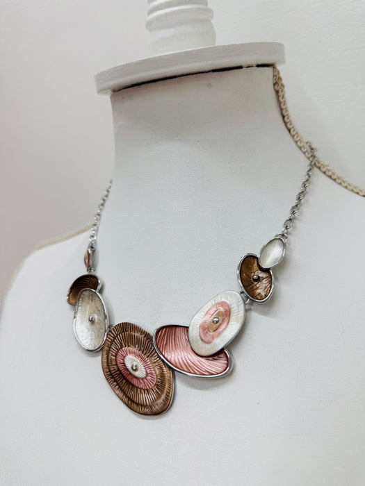 Geometric statement necklace with silver tone chain and enamelled oval elements in bronze and pearl shades displayed on a mannequin.