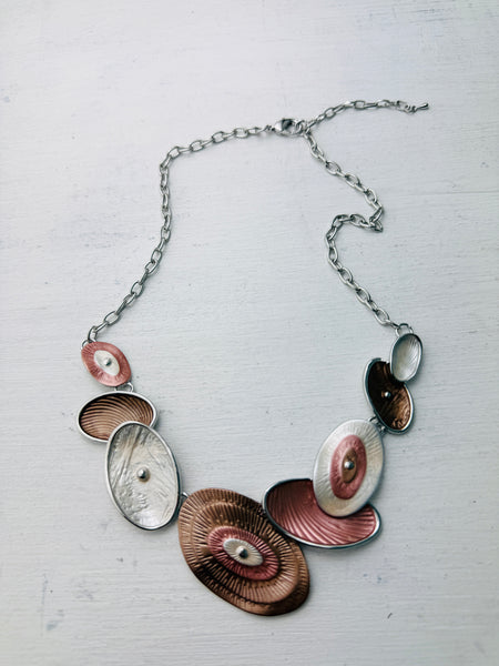 Geometric statement necklace with silver tone chain and enamelled oval elements in bronze and pearl shades displayed on a white background.