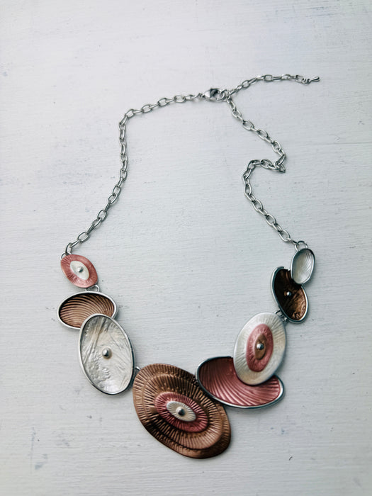 Geometric statement necklace with silver tone chain and enamelled oval elements in bronze and pearl shades displayed on a white background.