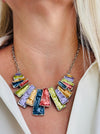 Multicoloured geometric statement necklace with rectangular enamel shapes in metallic gunmetal, bronze, gold, lilac and lemon green, displayed on a model.