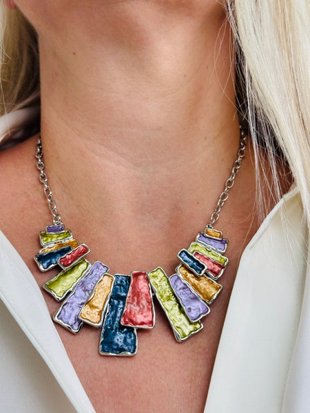 Multicoloured geometric statement necklace with rectangular enamel shapes in metallic gunmetal, bronze, gold, lilac and lemon green, displayed on a model.