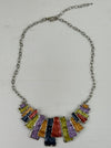 Multicoloured geometric statement necklace with rectangular enamel shapes in metallic gunmetal, bronze, gold, lilac and lemon green, displayed on a table.