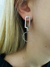 close-up of geometric silver drop earrings with rectangular and circular linked shapes