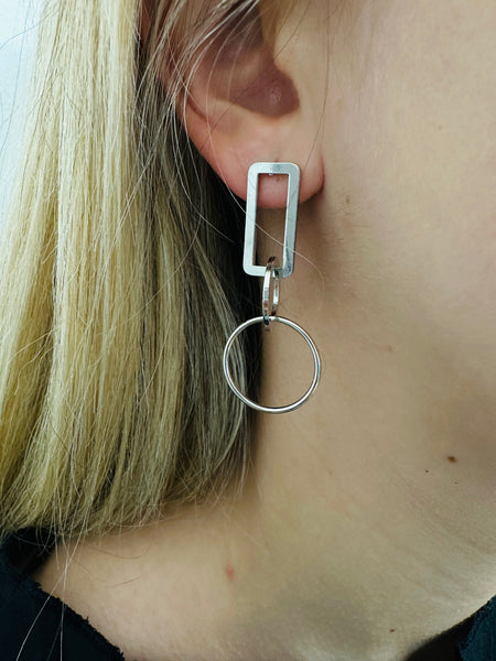 close-up of geometric silver drop earrings with rectangular and circular linked shapes