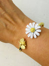A gold bracelet with a daisy and bee detail on a person's wrist.