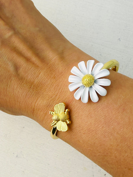 A gold bracelet with a daisy and bee detail on a person's wrist.