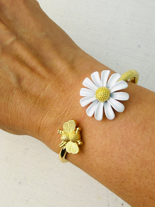 A gold bracelet with a daisy and bee detail on a person's wrist.