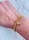 Gold bracelet with a heart-shaped charm on a wrist against a white background