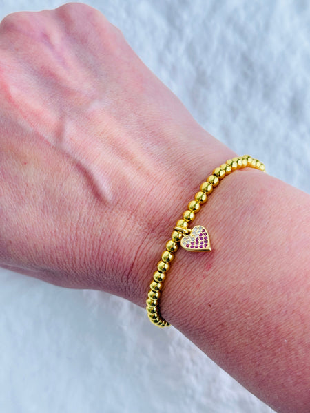 Gold bracelet with a heart-shaped charm on a wrist against a white background