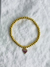 Gold beaded bracelet with a heart-shaped charm on a marble surface