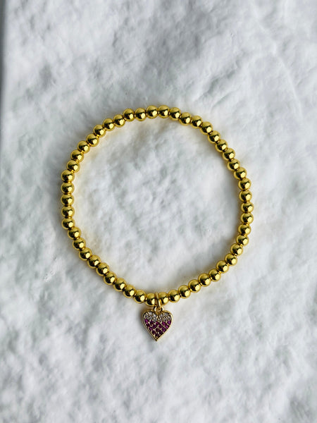 Gold beaded bracelet with a heart-shaped charm on a marble surface