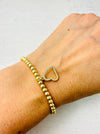 A gold bracelet with a crystal heart detail, displayed on a person's wrist.
