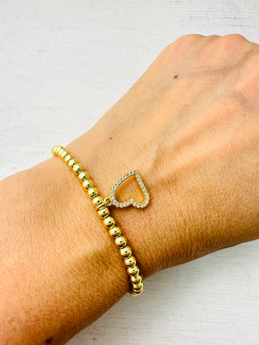 A gold bracelet with a crystal heart detail, displayed on a person's wrist.