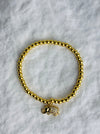 Gold beaded bracelet with a small elephant charm on a white marble surface