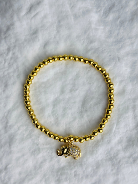Gold beaded bracelet with a small elephant charm on a white marble surface
