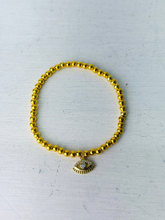 Gold beaded bracelet with a charm on a white background