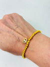 Gold beaded bracelet with an eye design on a wrist against a light background